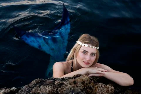 Mermaid swims in the water peeking out of the rocks. Photos