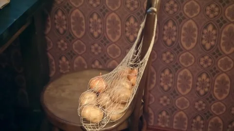 A mesh bag containing onions is hung on the back of a obsolete chair Stock Footage 323965548