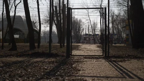 Mesh fence with a gate behind which people stroll through the park Stock Footage 303818277