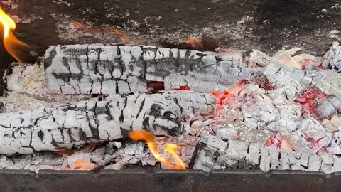 Mesmerizing flames over smoldering logs in a cozy outdoor campfire Stock Footage 303808000