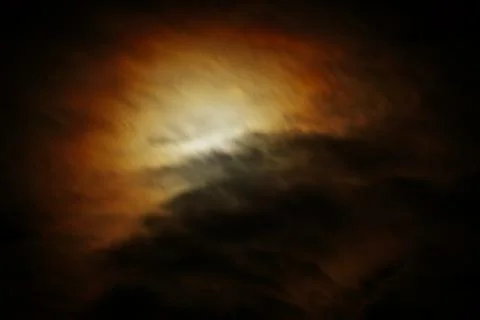 A mesmerizing full moon shines through fast-moving, illuminated clouds at night Stock Photos