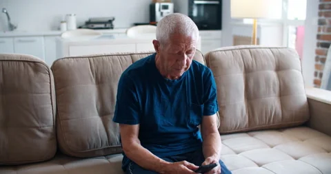 Message for children. An elderly man sits on the couch and writes a message on a Stock Footage 136387469
