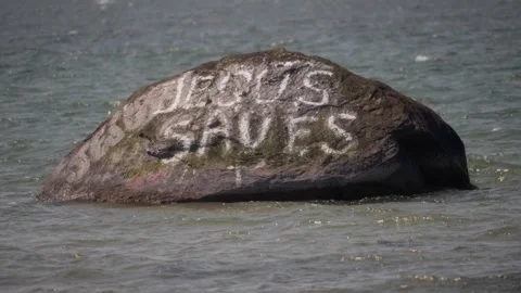 Message of grace in a tidal place, “Jesus Saves” on stone face Stock Footage 311508697