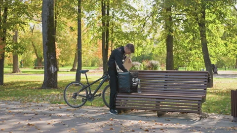 Messenger arranging takeout boxes beside park bench in autumn, Delivery person Stock Footage 329574825