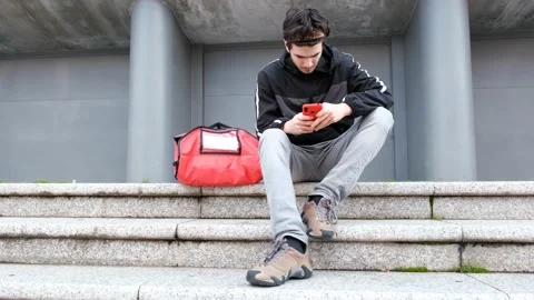 Messenger sitting down looking for order address on mobile phone Stock Footage 145849194
