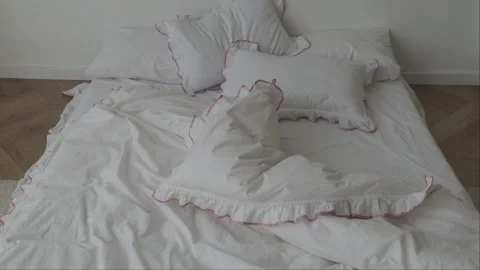 Messy bed with white bedding and pink ruffled pillows in cozy minimalist bedroom Stock Footage 310931046