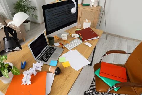 Messy home office desk with laptop, computer monitor, VR headset, and scatter Stock Photos