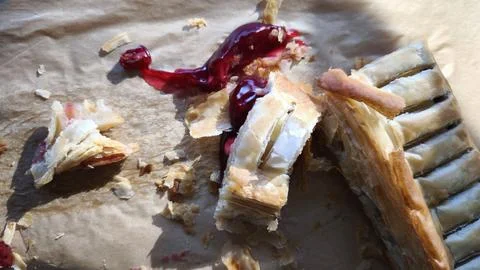 Messy leftovers of a flaky cherry puff pastry with crumbs. Close-up of a fi.. Stock Photos