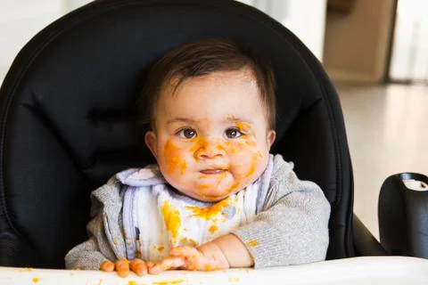 Messy Mixed race baby eating food in high chair Stock Photos