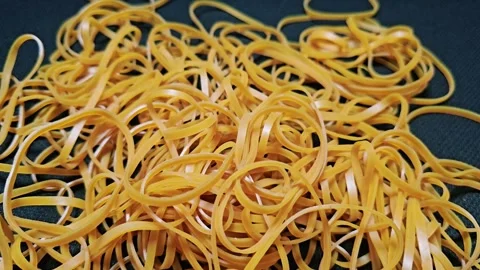 A messy pile of thin, beige rubber bands tangled together on a plain Video stock 345930076