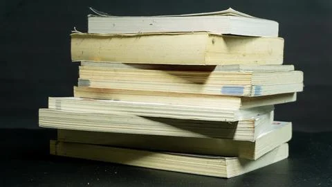 Messy stack of books with uneven alignment against black background, disorg.. Stock Photos