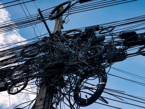 Messy tangled electrical power cables and wires on utility pole against blu.. Foto stock