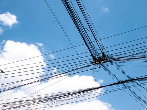 Messy Tangled Electrical Power Lines and Cables Against Blue Sky with Clouds 스톡 사진