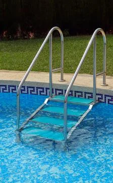Metal access steps in clear blue water of residential swimming pool near gr.. Stock Photos