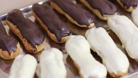 Metal backing tray with eclairs with chocolate and white icing, close-up Stock Footage 276364186
