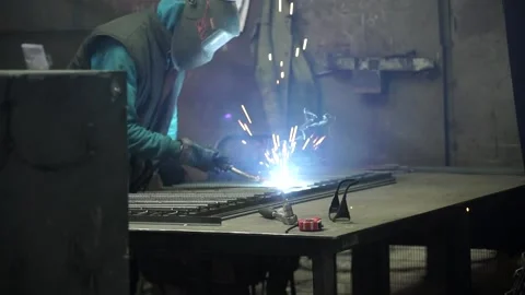 Metal bars lie on the table and the welder works with it. Stock Footage 196879478