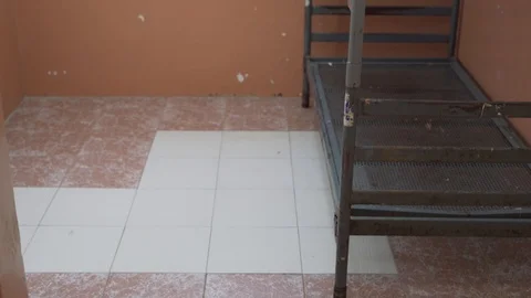 Metal bed in a prison cell on the background of a window with bars Stock Footage 120146206