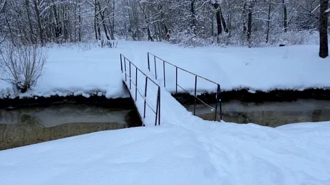 A metal bridge over a wild river in a winter forest, an unfrozen stream, a sandy Stock Footage 171670492