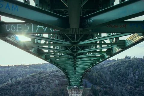 Metal bridge structure from below with rivets and sunlight above valley Stock Photos
