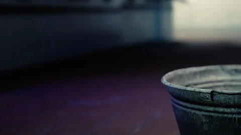 Metal bucket placed on the floor in a dimly lit room with blurred background Stock Footage 344858995