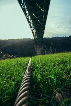 Metal cable on grass with perspective view of bridge above valley Stock Photos