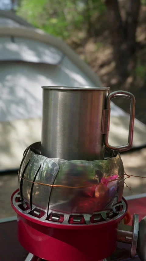 Metal Camping Mug Heating on Portable Gas Stove at Outdoor Campsite Stock Footage 341995554