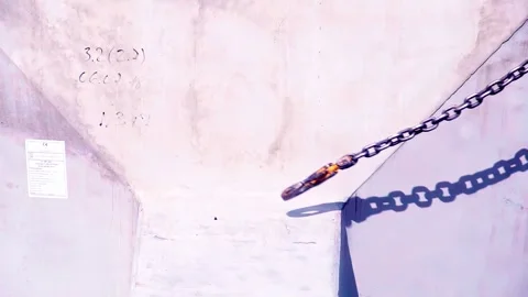 Metal chain with clevis hook being pulled upward casting shadow on wall Stock Footage 334671537