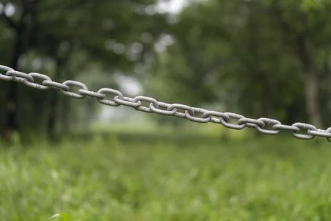 A metal chain squeezes across the background of grass and tree Stock Photos