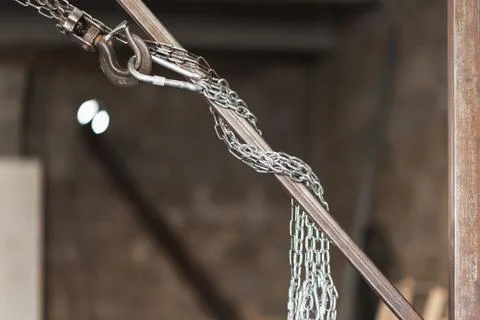Metal chains in a workshop hang from a rusty metal pipe Stock Photos