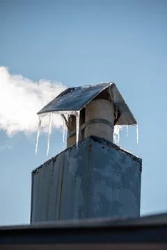 Metal chimney stack with icicles and winter steam 库存照片