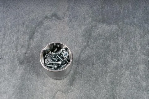 Metal container filled with assorted screws on gray surface Stock Photos