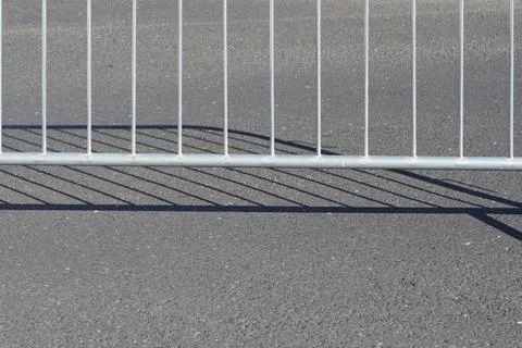 Metal crowd control barrier with shadow on asphalt road surface Stock Photos