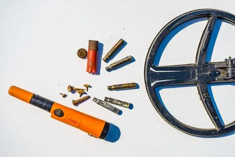 A metal detector, tools, and various small objects are arranged on a flat sur Stock Photos