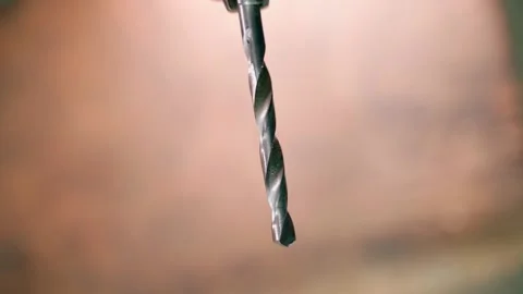A metal drill rotates close-up on a light brown background. Background from an Stock Footage 206433065