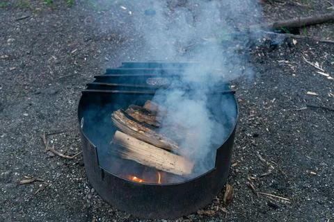 A metal fire pit glows with burning logs, sending smoke signals skyward. Stock Photos