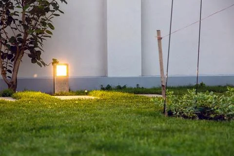 Metal floor lantern lighting the backyard trail with green plants. Stock Photos