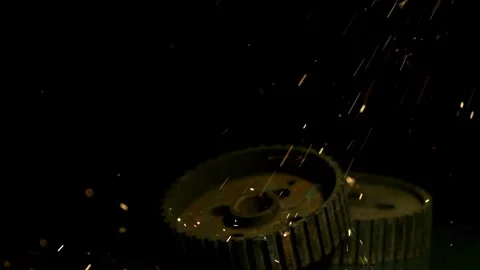 Metal gears on dark surface with falling orange sparks Stock Footage 327514296