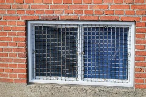 Metal grid protected basement window in red brick wall with concrete foundati Stock Photos