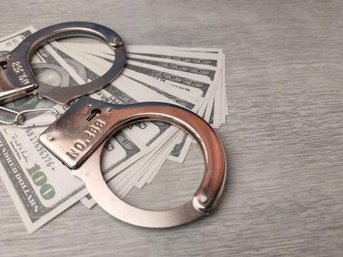 Metal handcuffs resting on top of a stack of US one-hundred-dollar bills Stock Photos