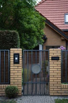 Metal intercom gate stands closed in a brick fence of a suburban house Stock Photos