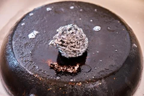 A metal kitchen sponge lies on a pan with a burnt bottom. Up close Stock Photos
