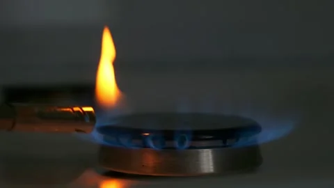 Metal lighter sets fire to burner of gas stove against dark background. Bright f Stock Footage 247498880