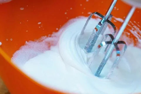 Metal mixer whisks beating a translucent egg white into a stiff white foam, s Stock Photos
