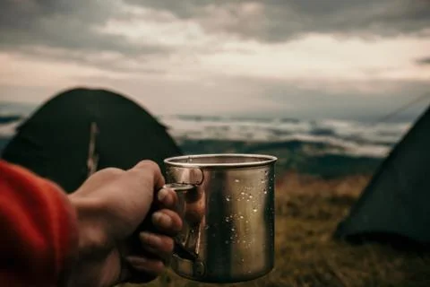 Metal mug with tea in hand of a tourist in tent camp in mountains Stock Photos