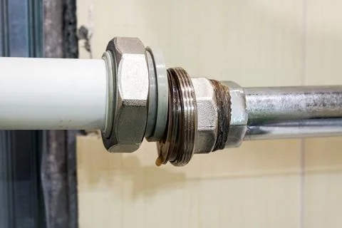 A metal nut and threaded fitting connecting a white plastic pipe to a steel.. Stock Photos