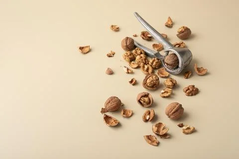 Metal nutcracker with scattered walnut shells and kernels on beige background Stock Photos