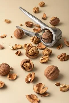 Metal nutcracker with scattered walnut shells and kernels on beige background Stock Photos