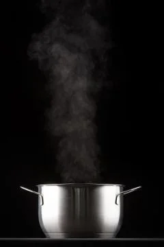 Metal pan on a black background, comes steam. Stock Photos