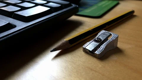Metal pencil sharpener lying next to striped pencil on sun lit table Stock-Footage 107605728