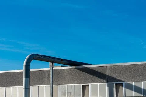 Metal pipe extends over the edge of a building under a clear blue sky Stock Photos